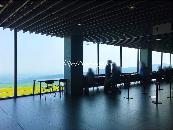 開放的なガラス窓から見える、広大な十勝平野。その景色を眺めながら食事をする観光客